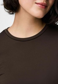 Top de tela marrón ajustado con una textura suave. Presenta un escote redondeado y mangas cortas, que muestran parte del cuello y la zona de la mandíbula.