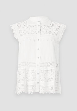 Blusa blanca con mangas cortas tipo capa, que presenta detalles de encaje y un frente abotonado. La tela texturizada y el dobladillo con forma de escallona añaden interés visual.