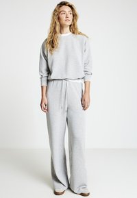 Felpa grigio chiaro e pantaloni a gamba larga abbinati in tessuto morbido. L'outfit presenta una vita con coulisse e polsini a coste ai polsi.