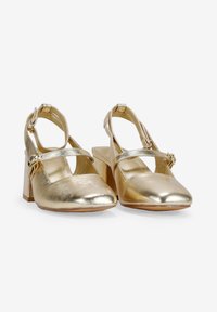 Zapatos de imitación de cuero dorado con punta afilada, correa en el tobillo y tacón cuadrado. Presentan acentos metálicos y una textura suave y brillante.