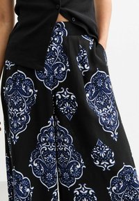 Schwarz gemusterte weite Hosen mit blauen und weißen, kunstvollen Designs, aus leichtem Stoff mit glatter Textur.
