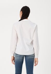 Hvit langermet skjorte med krage, med knappede mansjetter og en glatt tekstur, sammen med blå smale jeans.