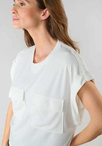 Top bianco a maniche corte con due tasche frontali, texture a costine e cuciture decorative sulla spalla. Tessuto morbido, vestibilità comoda.
