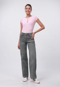 Top corto de manga corta en rosa claro con detalle de ojal, combinado con jeans de tiro alto gris de pierna ancha y zapatillas blancas con rayas negras.
