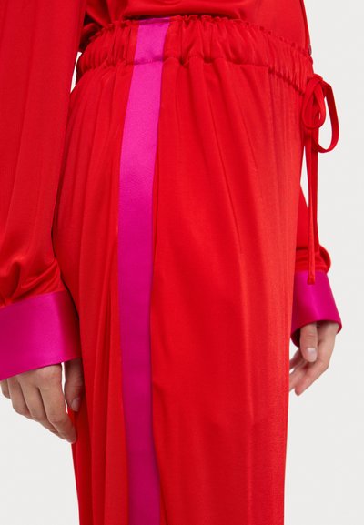 Pantalons rouges avec une taille à cordon, dotés de rayures latérales en satin rose et de larges manches, fabriqués à partir d'un tissu lisse et léger.
