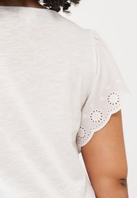 Close-up of a person's shoulder and upper back, wearing a white shirt with intricate lace detailing at the sleeve edge.