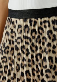 Plissierter Rock mit einem Leopardenmuster in Schwarz- und Brauntönen. Der Bund ist schwarz und hat einen dezenten Schimmer. Strukturierte Stoffpaneele erzeugen Volumen.