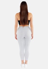 Szare legginsy o wysokim stanie z gładką fakturą, dopasowanym krojem i elastycznym materiałem, w połączeniu z czarnym topem crop i białymi sneakersami.