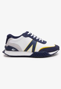 Zapatilla blanca con acentos en azul marino y amarillo, que cuenta con una suela texturizada, parte superior suave y diseño de cordones. Logo de Lacoste en el lateral.