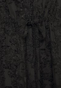 Vestido negro con detalles de aplicación floral texturizada. Cuenta con una cintura atada y una tela en capas que crea profundidad y movimiento. Base de material suave.