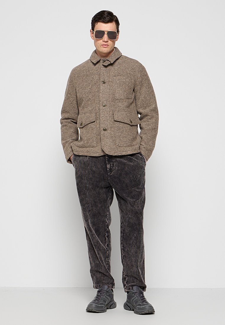 Braune Wollmischung Jacke mit Kragen, vorderen Taschen und Knopfverschluss, kombiniert mit grauen Cordhosen und schwarzen Sneakers.