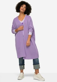 Ljuslila oversized cardigan med ribbad textur, öppen fram, och sänkta axlar, bärs över en randig topp och matchas med cropped jeans.