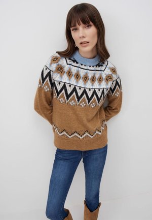 Maglione marrone lavorato a maglia con colletto a coste blu, caratterizzato da motivi geometrici in nero, bianco e beige. Abbinato a jeans blu e stivali marroni.