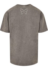 Grijze oversized t-shirt met een vervaagde textuur, voorzien van een wit vlinderontwerp op de bovenrug en een klassieke ronde hals.