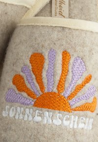 Felt slippers feature a sunrise design in orange, purple, and white embroidery on a beige background. Soft texture with cream trim.