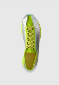 Scarpa sportiva verde brillante e argento con lacci gialli vista dall'alto su uno sfondo chiaro e semplice.