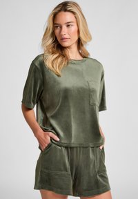Olijfgroene lounge-outfit gemaakt van zachte, gestructureerde stof. Bevat een top met korte mouwen en een zak, en bijpassende shorts met voorzakken.
