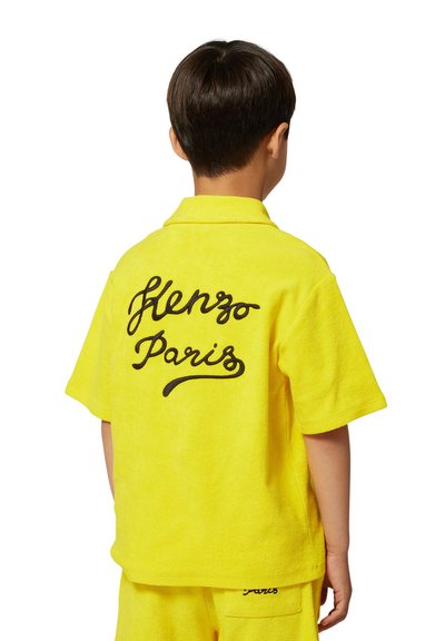 Maglietta gialla a maniche corte con texture, con un logo ricamato nero "Kenzo Paris" sulla schiena. Abbinata a pantaloni corti coordinati.