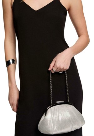 Donna che indossa un vestito nero senza maniche tiene una borsa metallica argentata con tracolla a catena e indossa un bracciale rigido e anelli d'argento.