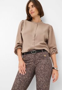 Beige blouse met knopen en puffmouwen, gecombineerd met bruine jeans met luipaardprint en een zwarte riem. Soepele stoftextuur, casual ontwerp.