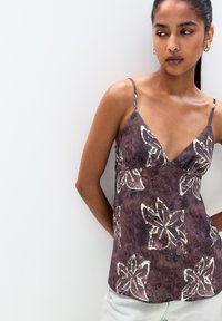 Brown floral print camisole with thin adjustable straps, featuring a v-neckline and a relaxed fit. Fabric appears lightweight and textured.