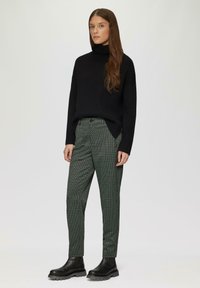 Pull en col roulé noir, coupe ample. Pantalons verts à pois blancs. Bottines noires à semelles épaisses. Design simple et moderne.