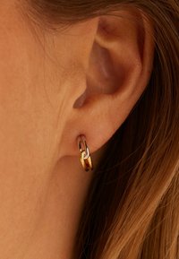 Gouden en zilveren met elkaar verbonden oorringen met een gepolijste afwerking, weergegeven op de oorgang nabij een persoon zijn oor.