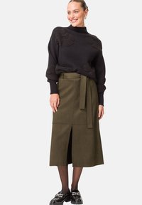 Czarny sweter dzianinowy z teksturowymi akcentami i wysokim kołnierzem, w zestawieniu z oliwkowo-zieloną spódnicą z zamszu o wysokim stanie, z rozcięciem z przodu i paskiem do związania.