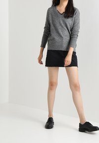 Szary sweter w serek z długimi rękawami, noszony na czarną dżinsową mini spódniczkę. Całość uzupełniają czarne sznurowane buty. Gładka, miękka tekstura.