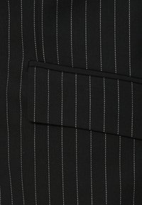 Μαύρο ύφασμα με λευκές κάθετες ρίγες έχει μια μόνο πλαϊνή τσέπη. Η υφή φαίνεται λεία με κομψό σχέδιο.