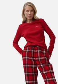 Top rojo de manga larga con "Ho Ho Ho" bordado en blanco, combinado con pantalones de cuadros rojos con líneas negras y blancas. Textura de tela suave.