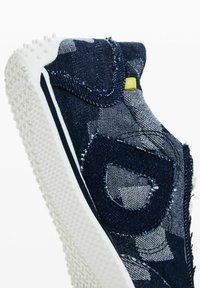 Sötétkék farmer slip-on cipő texturált anyaggal, ellentétes varrással és fehér gumitalppal, amely kis tapadó bumpokkal rendelkezik.
