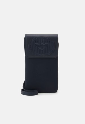 Lille mørkeblå crossbody taske med klaplukning og præget logo foran, med en tynd rem til at bære.