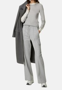 Suéter gris con detalles en crema, combinado con pantalones de pierna ancha gris claro con bolsillos y cintura ajustable; completado con un abrigo largo gris.