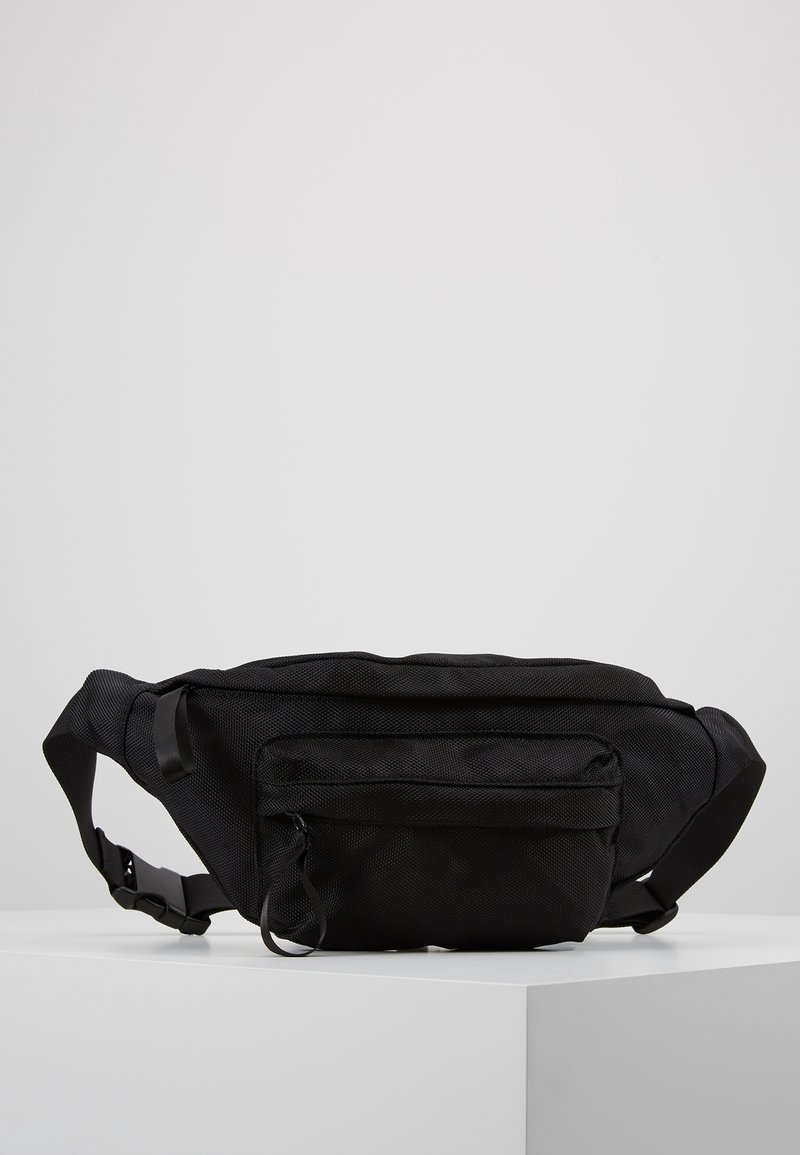 Riñonera negra texturizada con correa ajustable, que cuenta con un bolsillo delantero con cremallera y un diseño suave y redondeado. Material ligero.
