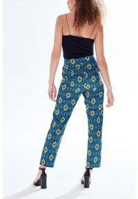 Blue patterned trousers with yellow diamond shapes, high-waisted design, straight leg, paired with a black fitted top and heels.