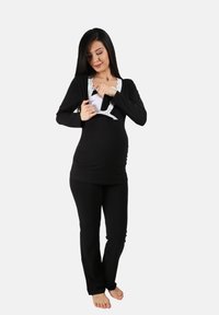 Blusa de maternidad negra con encaje y mangas largas, combinada con pantalones negros. La blusa cuenta con una abertura de acceso para la lactancia.