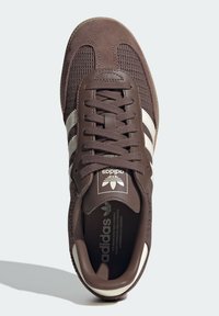 Scarpa sportiva marrone realizzata in mesh e suede, con punta rotonda, design con lacci piatti e marchio in bianco con tre strisce sui lati.