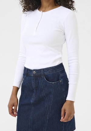 Femme portant un haut henley blanc ajusté à manches longues, rentré dans une jupe en jean bleu foncé taille haute avec des poches à l'avant.