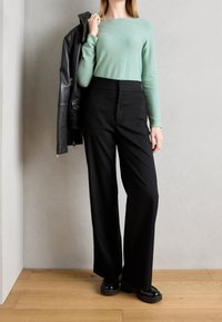 Mintgrünes Langarmshirt kombiniert mit hoch taillierten schwarzen weiten Hosen und klobigen schwarzen Schuhen. Das Model h�ält eine schwarze Lederjacke.