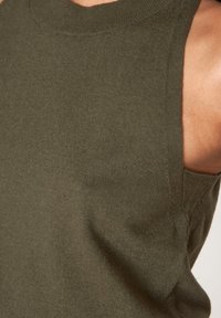 Top maglia senza maniche di colore verde oliva con scollo rotondo, tessuto morbido e aperture laterali per la ventilazione. Dettagli delle cuciture visibili.