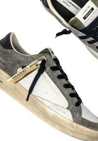 Sneaker in pelle grigia e bianca con lacci neri, suole textured beige e branding "Crime London" sul lato e sulla linguetta.