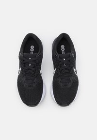 Chaussures de sport noires avec un dessus en tissu texturé, des lacets noirs et des accents blancs sur la semelle. Comprend un logo rond sur la languette.