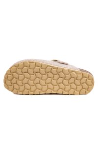 Semelle d'un chausson en feutre beige avec une semelle en caoutchouc texturé présentant un motif en vagues pour une meilleure adhérence et un talon légèrement surélevé.