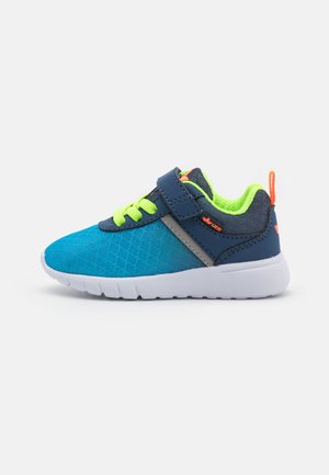 A kék sportcipő texturált felsőrésszel rendelkezik, kontrasztos tengerészkék részletekkel, neon zöld fűzőkkel és fehér gumitalppal, amely tapadási barázdákkal van ellátva.