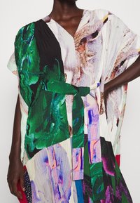 Robe kaftan multicolore avec des motifs abstraits, un décolleté en V, des manches courtes et une ceinture en tissu vert, fabriquée en matériau texturé léger.