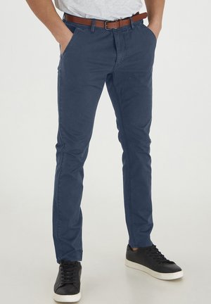 Chino blu navy, in cotone, slim fit, design a cinque tasche, abbinati a sneakers nere e cintura in pelle marrone per contrasto.