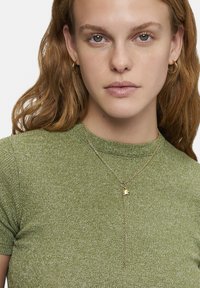 Guldhalsband med hänge, parat med en åtsittande, texturerad grön topp med rund halsringning och korta ärmar.