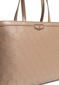 Beige syntetisk taske med præget logomønster, flad bund og dobbelte skulderstropper. Har en guldbelagt mærkeplade foran.