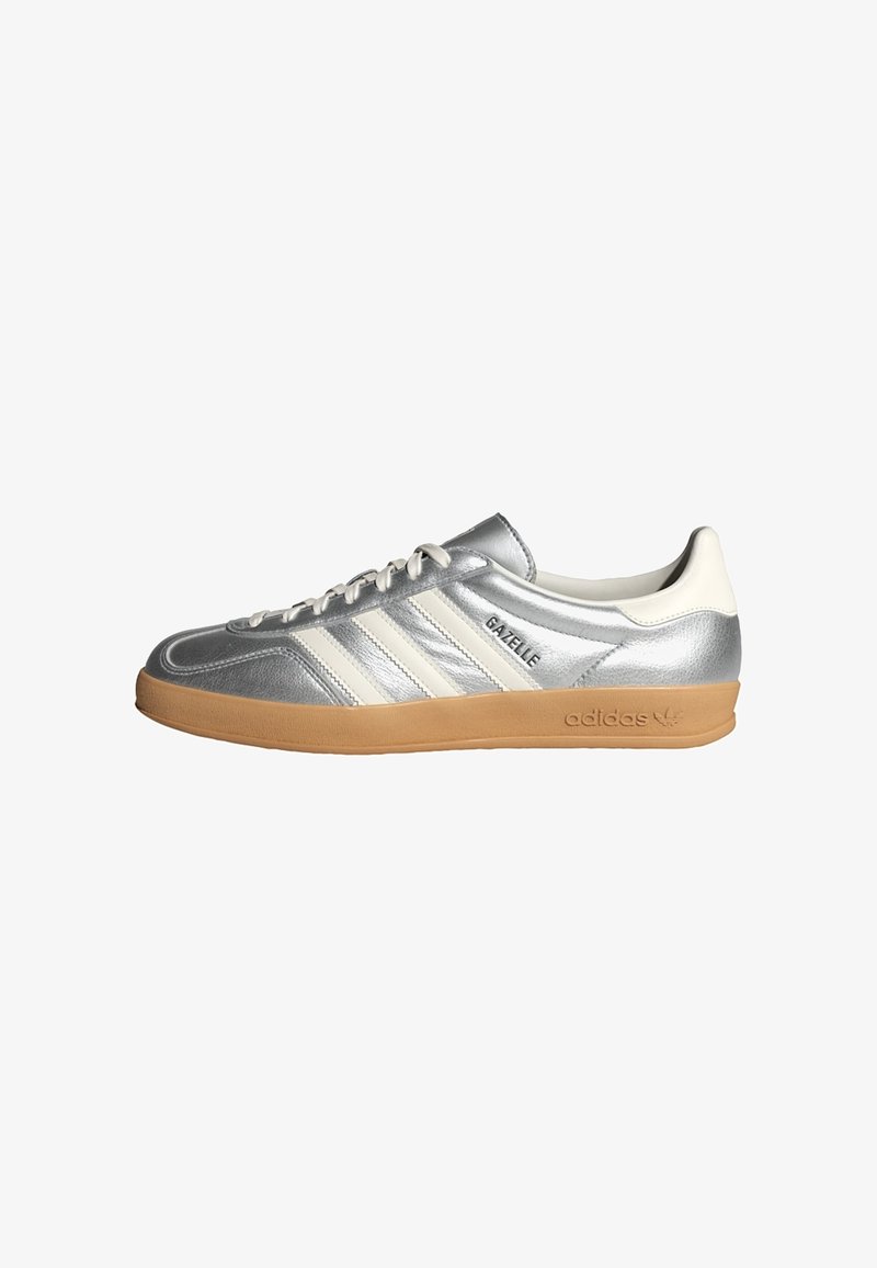 Silver Adidas Gazelle sneaker with white stripes, gum sole, and "Gazelle" text on the side, shown from the inner side.